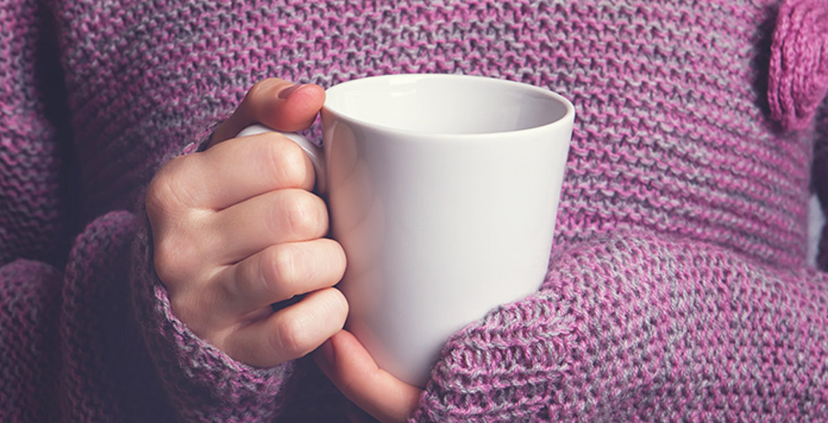 Frau in lilafarbenem Wollpullover hält eine Tasse Tee in beiden Händen