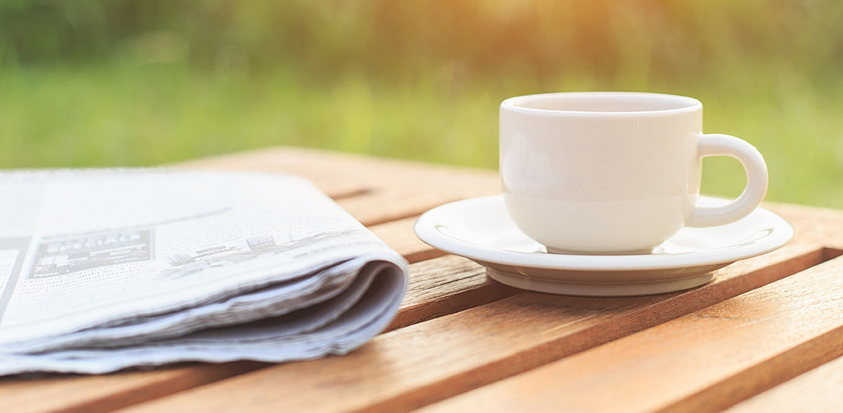 Eine Teetasse und eine Zeitung liegen auf einem Gartentisch
